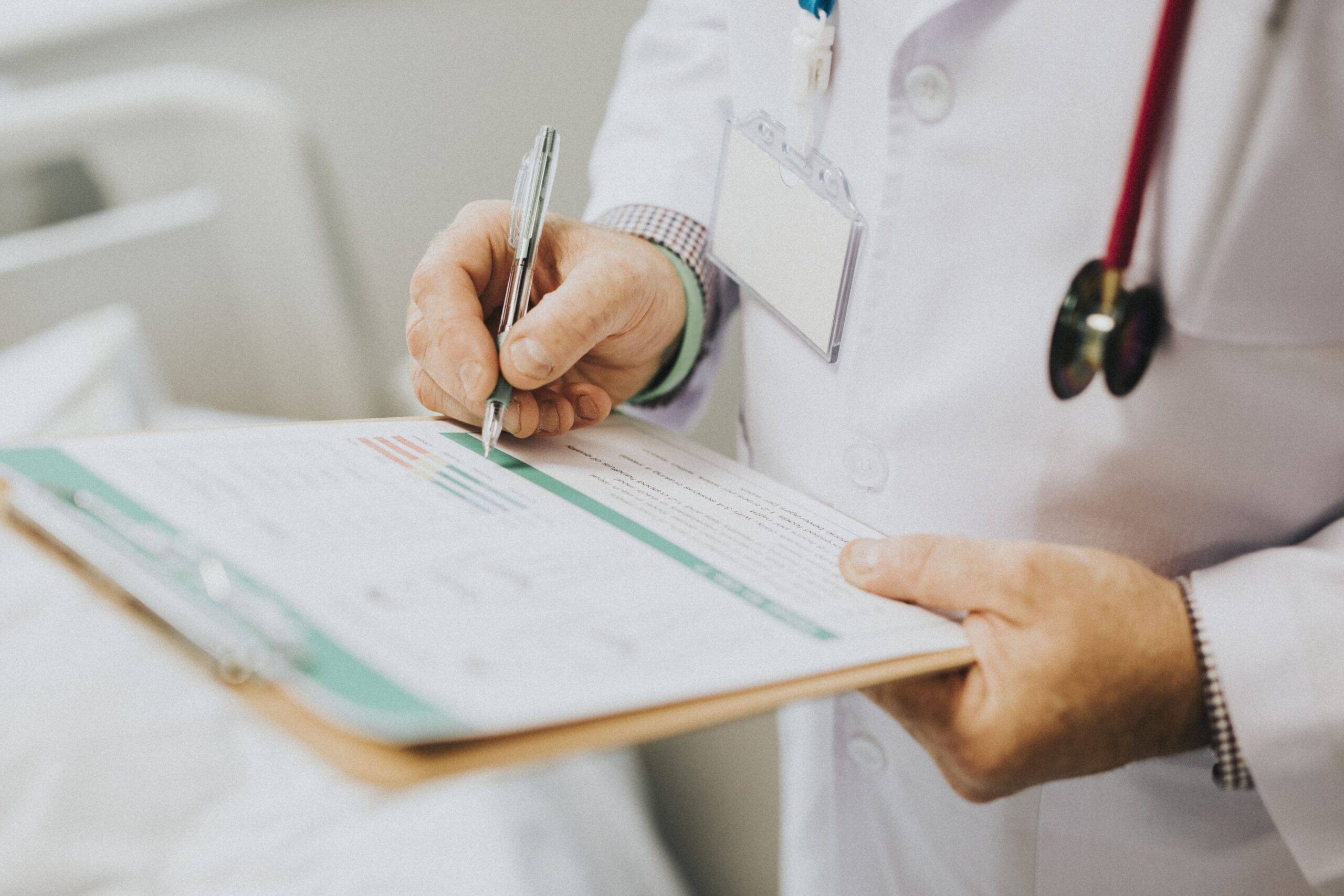 Médico preenchendo um formulário em uma prancheta durante atendimento, com estetoscópio ao fundo, representando consulta médica, prontuário ou documentação clínica.
