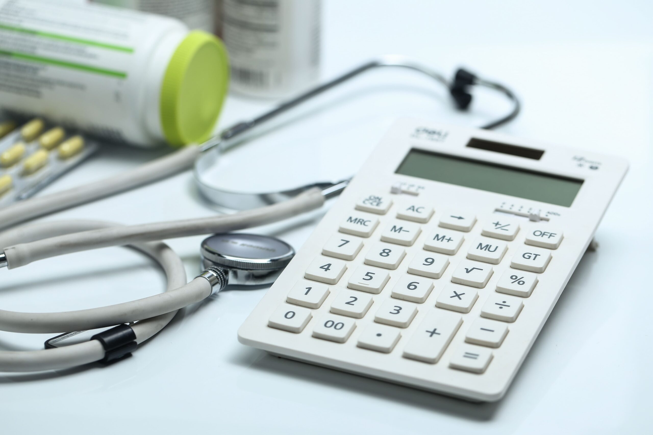 Estetoscópio, medicamentos e calculadora sobre uma mesa, representando custos de saúde, despesas médicas ou planejamento financeiro hospitalar.