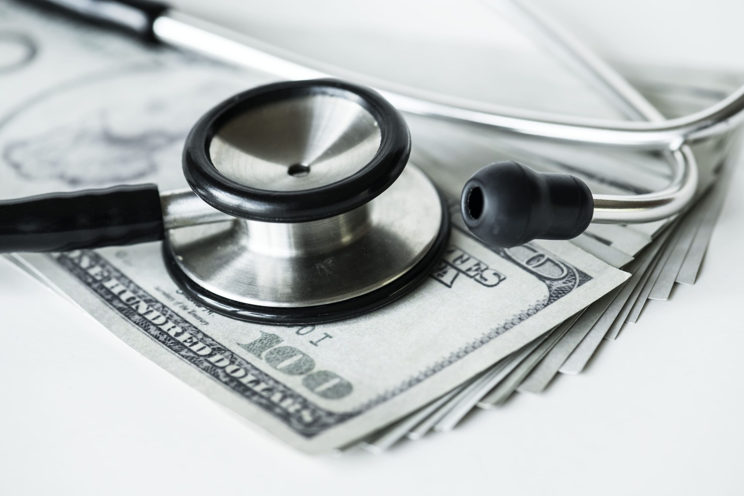 Estetoscópio em close sobre notas de dólar, representando custos médicos, despesas hospitalares ou finanças na área da saúde.