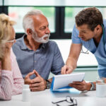Médico orientando casal de idosos durante consulta sobre plano de saúde para terceira idade.